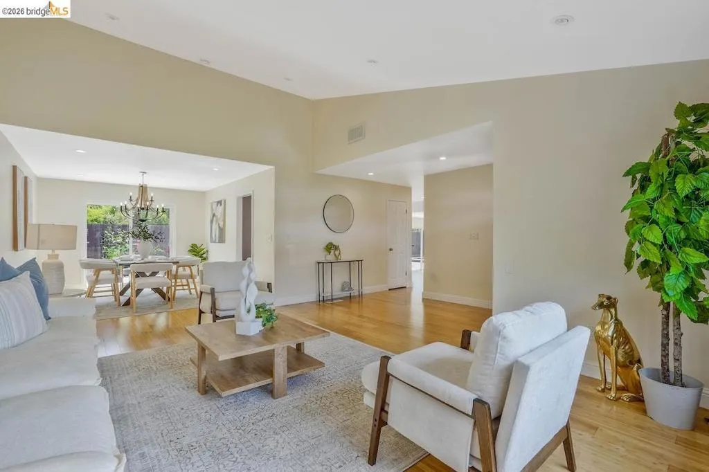 Spacious living area featuring polished wood-finish flooring, a neutral color palette, recessed lighting, and a large open doorway to an additional room