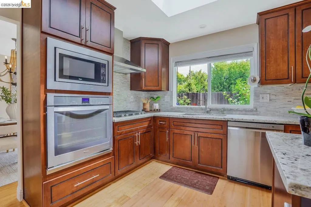 Kitchen featuring rich wood cabinetry, stainless steel appliances, light-toned countertops, a full backsplash, and a skylight