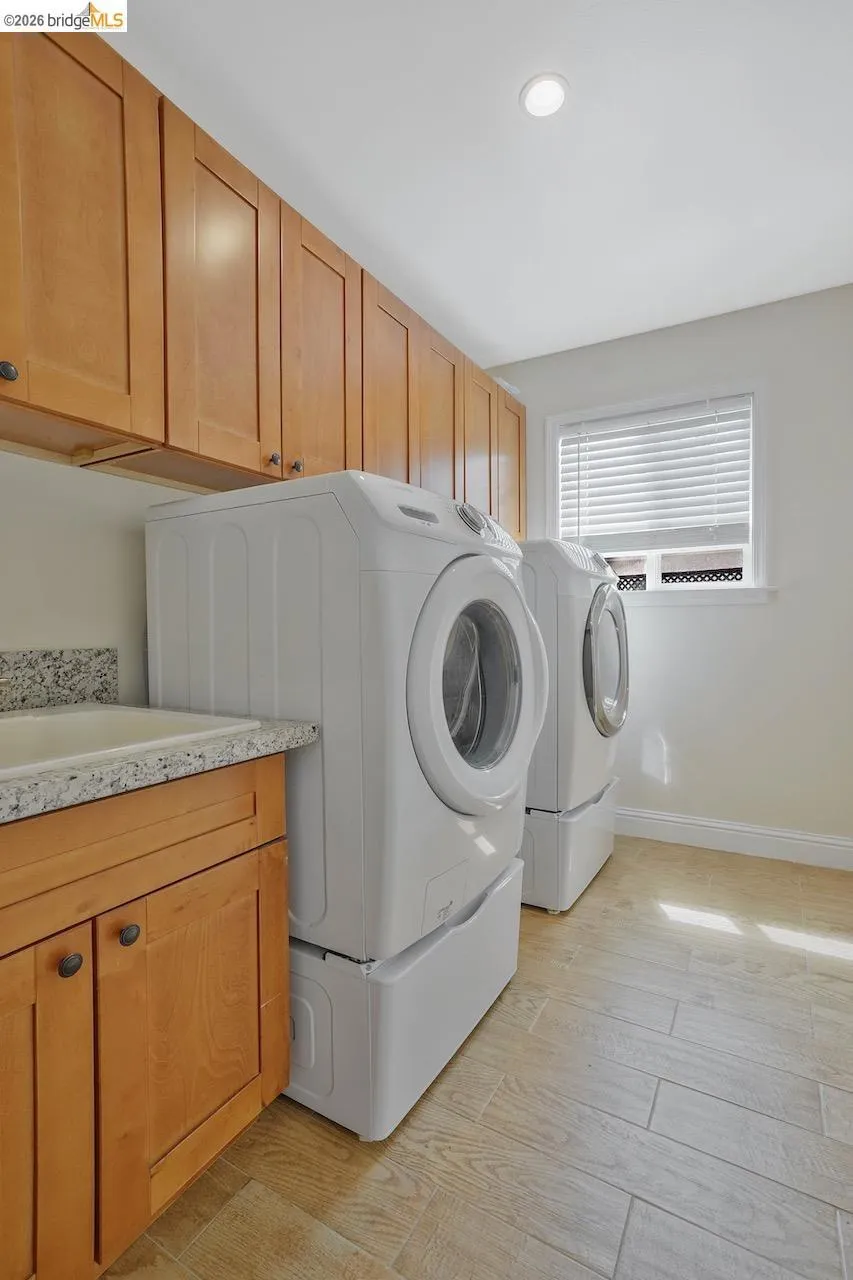 Laundry room featuring extensive wood cabinetry, a built-in utility sink with stone-finish countertop, wood-finish flooring, and recessed ceiling lighting