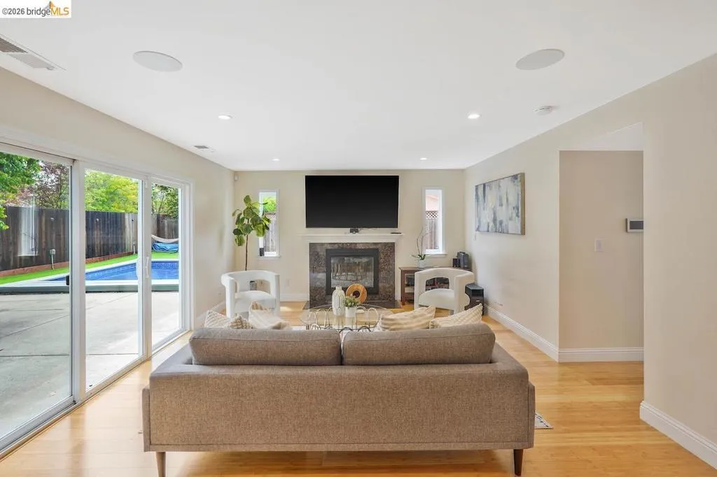 Living area featuring hardwood flooring, a fireplace with a stone surround, recessed lighting, and sliding glass doors opening to a backyard with a swimming pool
