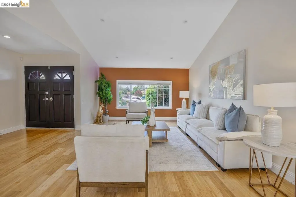 Spacious living area featuring light wood-finish flooring, a contemporary accent wall, and a large front window