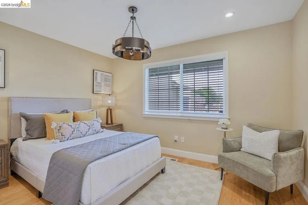 Bedroom featuring a modern chandelier, light wood-finish flooring, recessed lighting, a window with horizontal blinds, and neutral wall tones