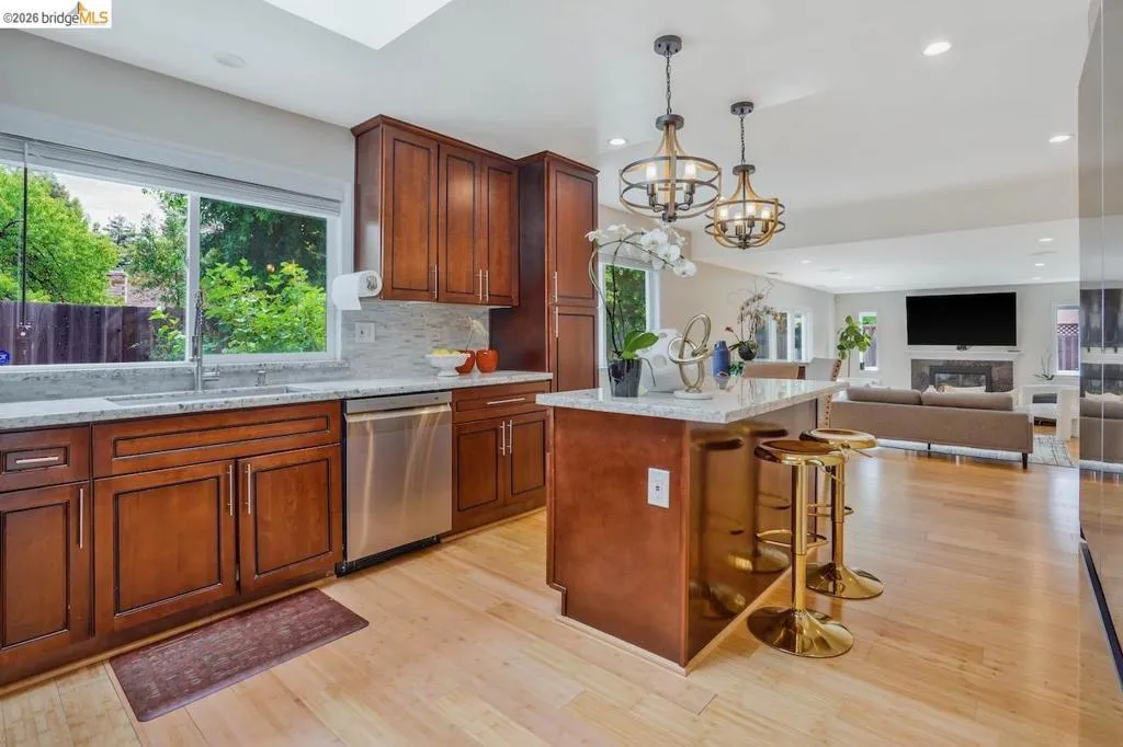 Open-concept kitchen featuring light wood-finish flooring, rich wood cabinetry, stainless steel appliances, and a skylight