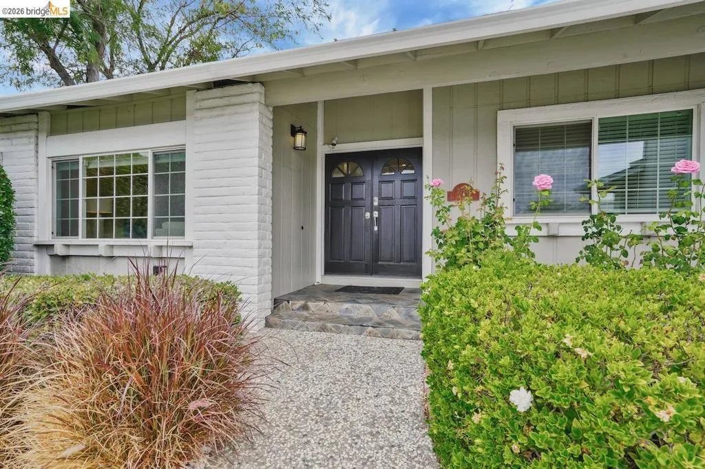 Front entryway featuring a double door with decorative glass inserts, stone steps, and an exposed aggregate walkway