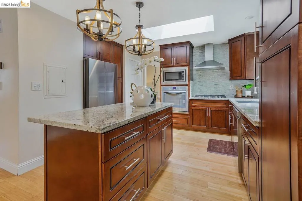 Kitchen with natural wood-finish flooring and a central island featuring a light-toned granite countertop