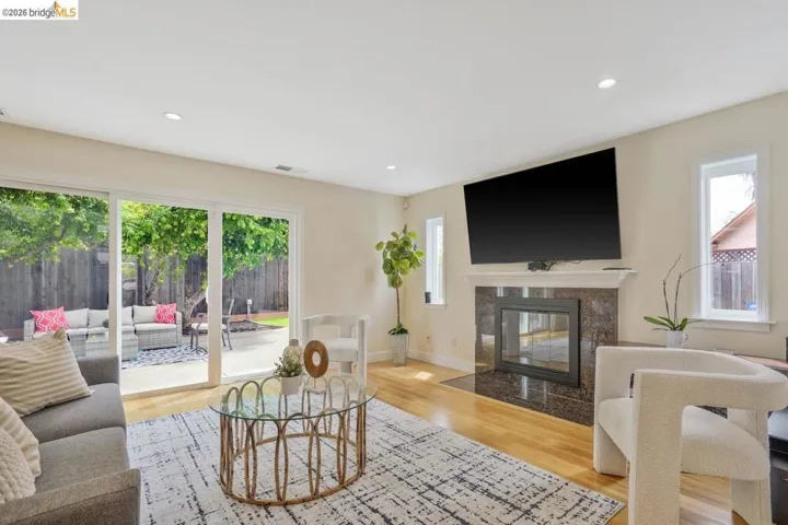 Living space featuring hardwood flooring, a fireplace with a stone surround, recessed lighting, and sliding glass doors opening to a backyard patio