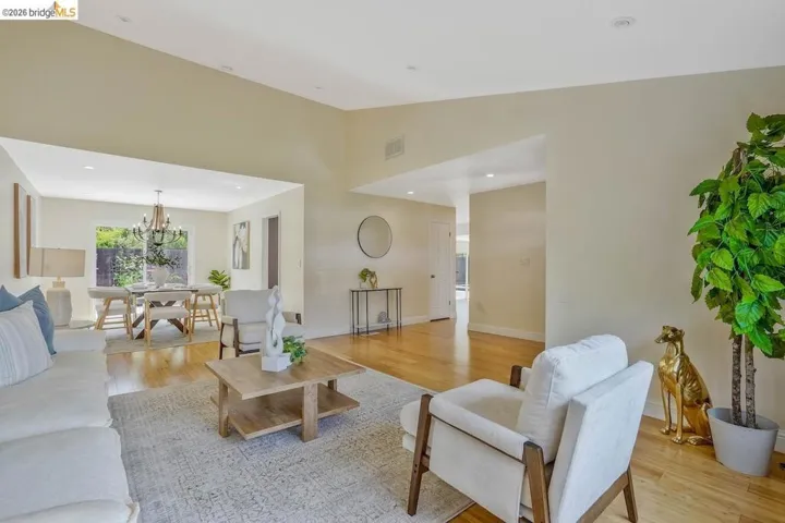 Spacious living area featuring polished wood-finish flooring, a neutral color palette, recessed lighting, and a large open doorway to an additional room