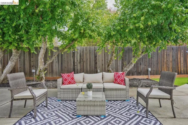 Spacious concrete patio area featuring a privacy fence, mature trees, and a landscaped border
