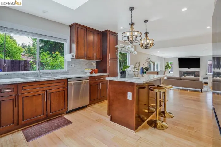 Open-concept kitchen featuring light wood-finish flooring, rich wood cabinetry, stainless steel appliances, and a skylight