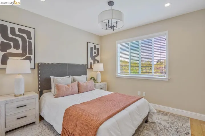 Recessed lighting illuminates this room featuring a ceiling-mounted drum chandelier, wood-finish flooring, and a large window with horizontal blinds