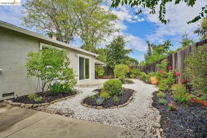 Landscaped backyard featuring a pea gravel pathway, raised garden beds with dark mulch, and a wooden privacy fence