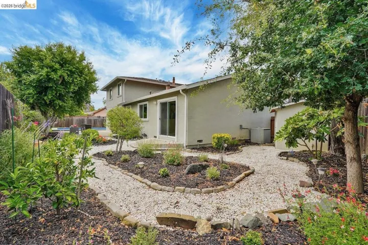Landscaped backyard featuring light-colored gravel paths, defined planting beds, mature trees, and a stucco exterior with sliding glass doors