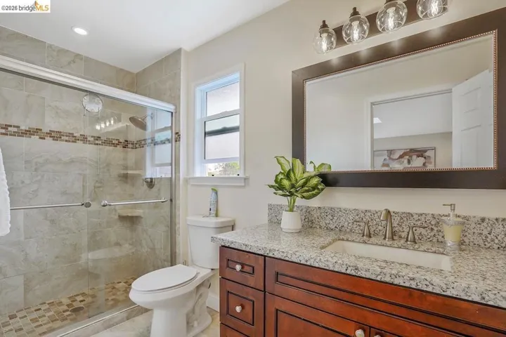 Bathroom featuring a glass-enclosed shower with tile surround and mosaic accent, a vanity with granite countertop and undermount sink, rich wood-tone cabinetry, and a mirrored vanity light fixture