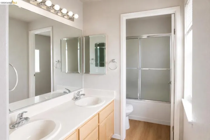 Bathroom featuring a dual vanity with light wood-finish cabinetry and chrome fixtures, illuminated by a strip of vanity lighting