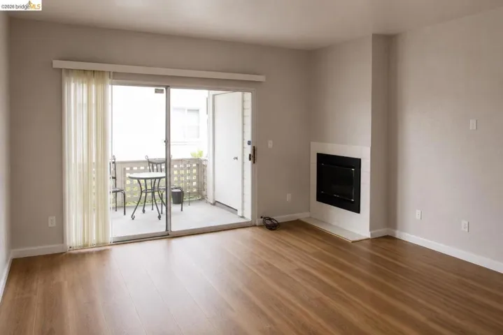 Spacious living area featuring wood-finish flooring, a contemporary fireplace with a white tile surround, and direct access to an outdoor patio via a sliding glass door