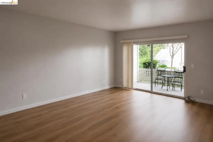 Spacious interior room with wood-finish flooring, light-toned walls, and white baseboards