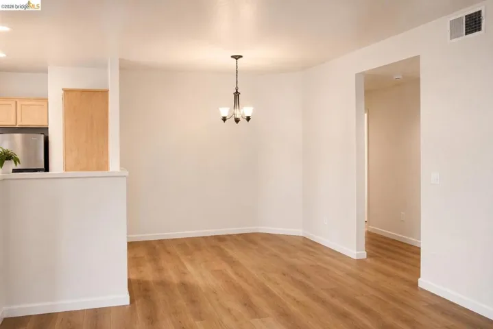 Open-concept dining area featuring wood-finish flooring, a contemporary chandelier, and a partial wall separating the kitchen