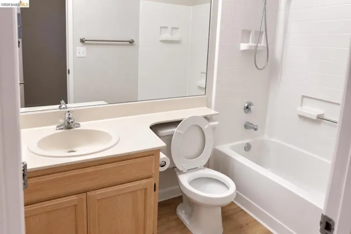 Bathroom featuring a light wood-finish vanity with an integrated sink, a neutral-toned countertop, a full-width vanity mirror, a toilet, and a bathtub with white subway tile-style surround