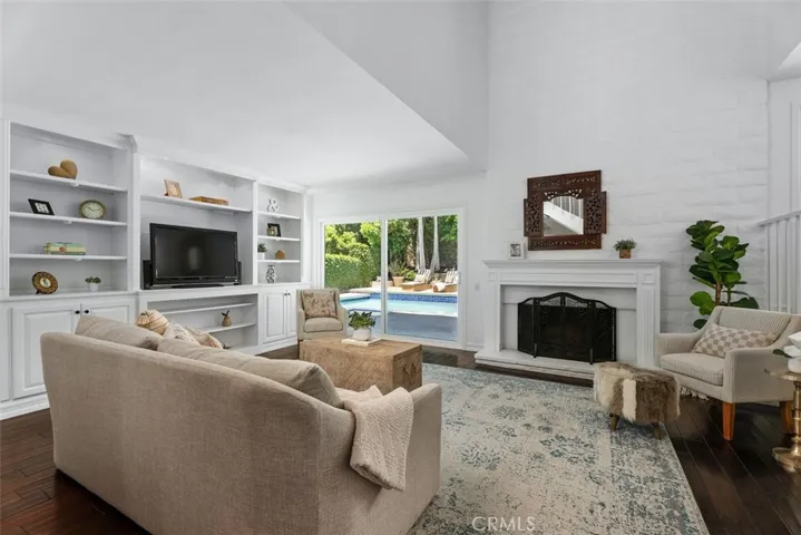 A closer perspective of the family room highlights the rich hardwood flooring, custom white shelving, and expansive pool views, offering a relaxing retreat.