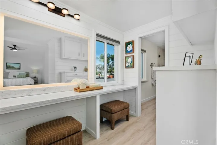 The primary suite includes a dedicated dressing area featuring a long marble vanity counter, chic shiplap walls, a light-up mirror, and cushioned stool seating.