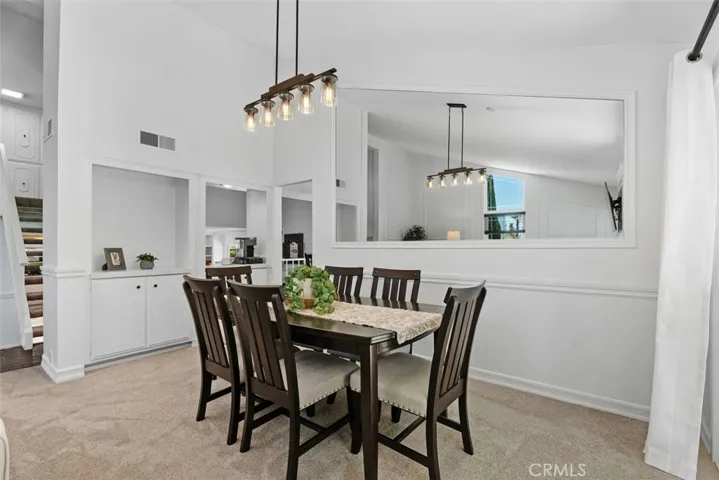 Centered under a modern rustic chandelier, the formal dining area features a large inset wall mirror that enhances the room's airy, light-filled atmosphere.