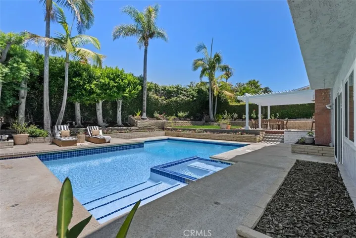 This beautifully maintained pool area is framed by majestic palm trees and lush privacy hedges, creating a peaceful, resort-style retreat.