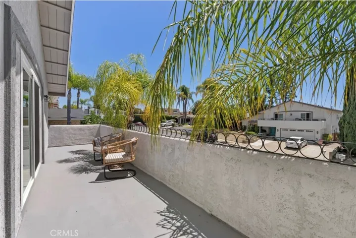 Just outside the primary suite onto this spacious, private deck featuring a durable surface, classic wrought-iron railing, and palm tree views.