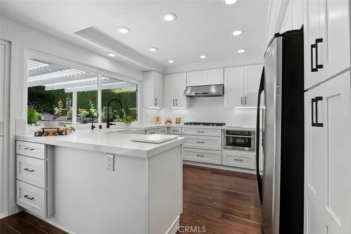 This chef-inspired kitchen features custom white cabinetry, crisp quartz countertops, and windows framing serene views of the outdoor pergola.