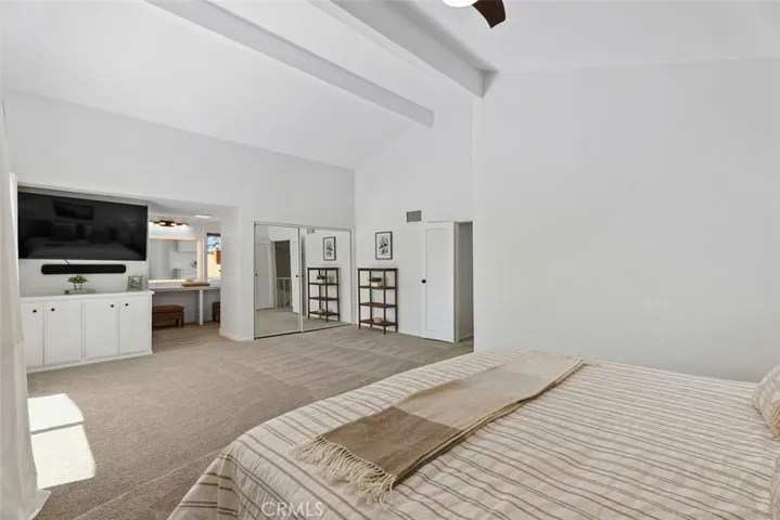 A wide angle of the primary suite highlights the dramatic vaulted ceilings, mirrored closet doors, and seamless flow into the vanity area.