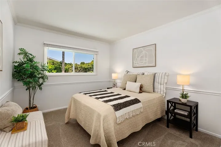 Another comfortable bedroom offering cozy carpeted flooring, classic chair rail molding, and a bright window with views of the surrounding greenery.