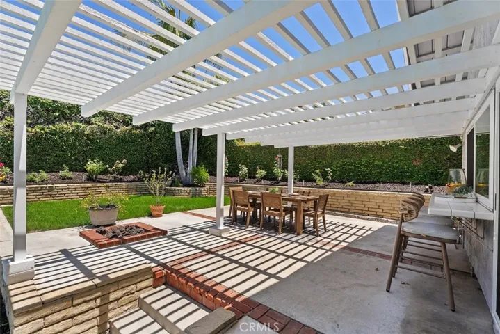 Perfect for hosting weekend gatherings, this shaded patio setup includes a fully equipped bar counter, a built-in brick fire pit, and direct access to the grassy lawn.