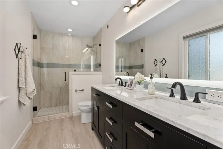 A beautifully upgraded primary bathroom showcasing a dark double vanity with a marble countertop, custom black fixtures, and a glass-enclosed walk-in shower.