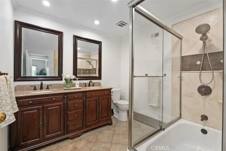 The upstairs spacious full bathroom boasts a double-sink wood vanity with granite countertops, dual framed mirrors, and a tiled tub-and-shower combination.