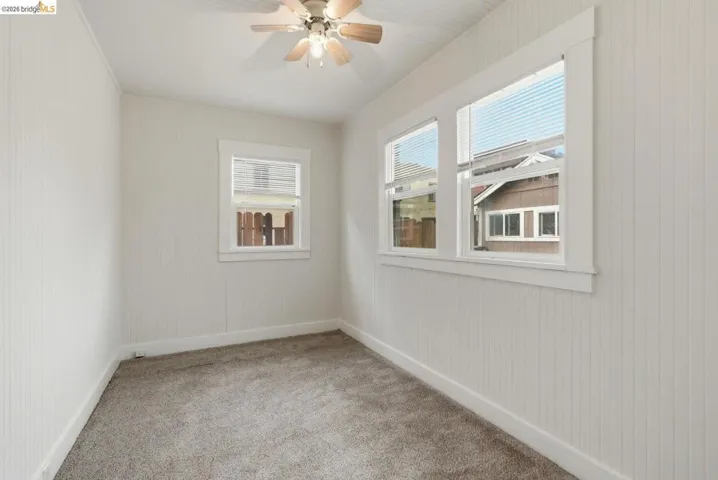 Room featuring white vertical plank walls, neutral carpet, and a ceiling fan with light fixture