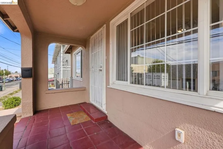 Covered front porch featuring red tile flooring, stucco exterior, multiple pane windows with security bars, and a security screen door