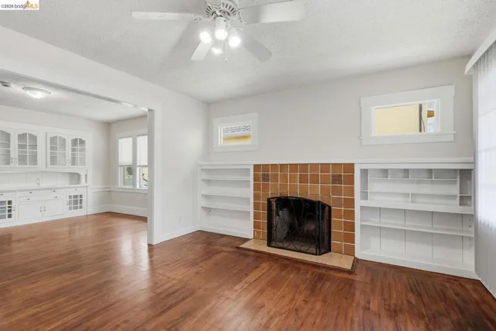 Living area featuring wood-finish flooring, a ceiling fan with integrated lighting, and a tiled fireplace hearth with a metal screen