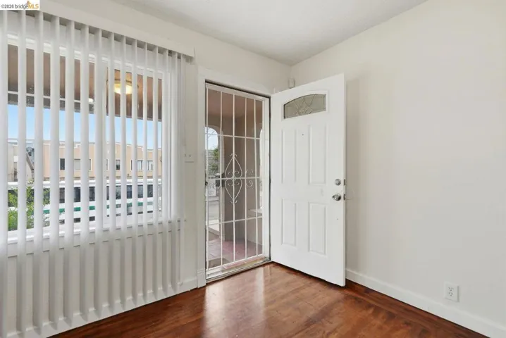 Entryway featuring a white paneled door with an arched glass insert, security screen door, wood-finish flooring, and vertical blinds on the window
