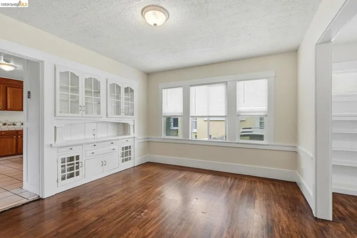 Spacious room featuring rich wood-finish flooring, a built-in white hutch with glass-front cabinetry, multiple windows, and a flush-mount ceiling light fixture