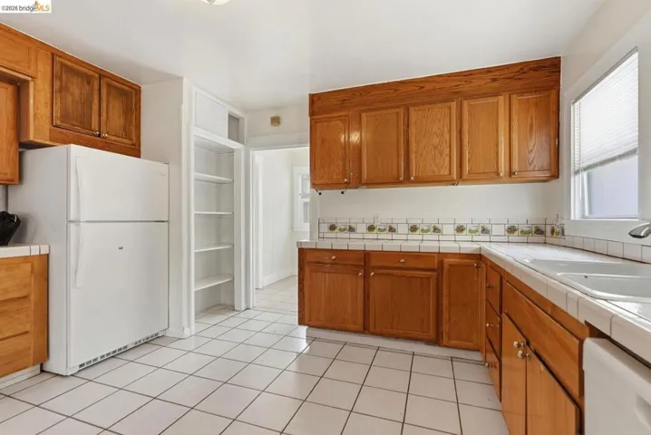 Kitchen featuring wood cabinetry, white tile flooring, white tile countertops, white tile backsplash with decorative accents, and a built-in pantry