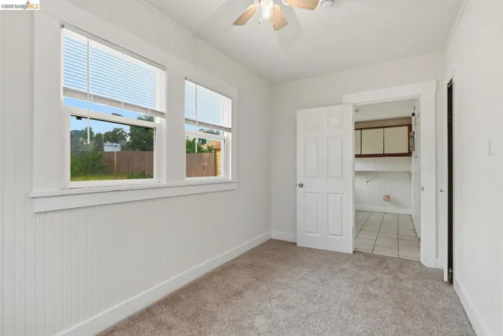 Room featuring two windows with blinds, white panel wainscoting, and neutral-toned carpeting