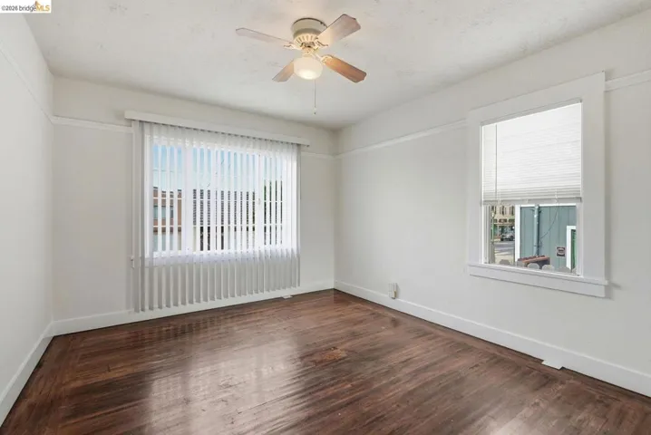 Room featuring rich wood-finish flooring, white painted walls, and a ceiling fan with integrated lighting
