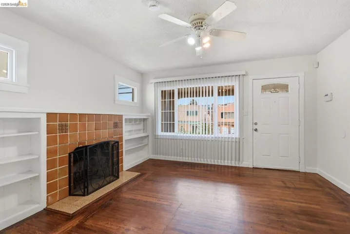 Living area featuring rich wood-finish flooring, a tile-surround fireplace with a hearth, and built-in shelving