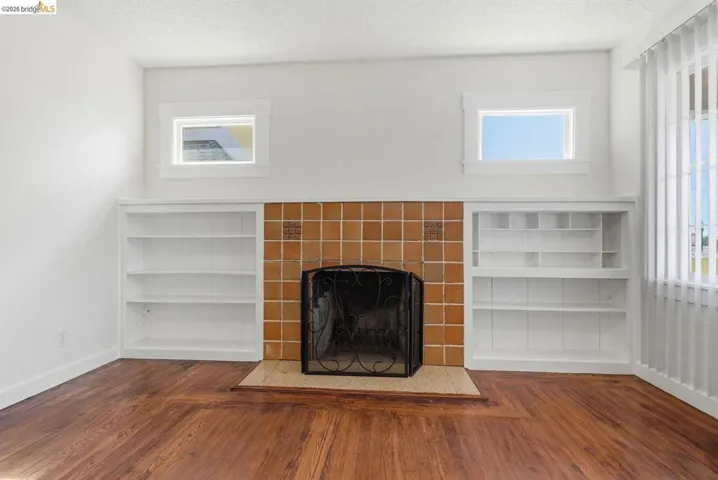 Fireplace featuring tan square tile surround and black metal screen, flanked by two built-in white shelving units