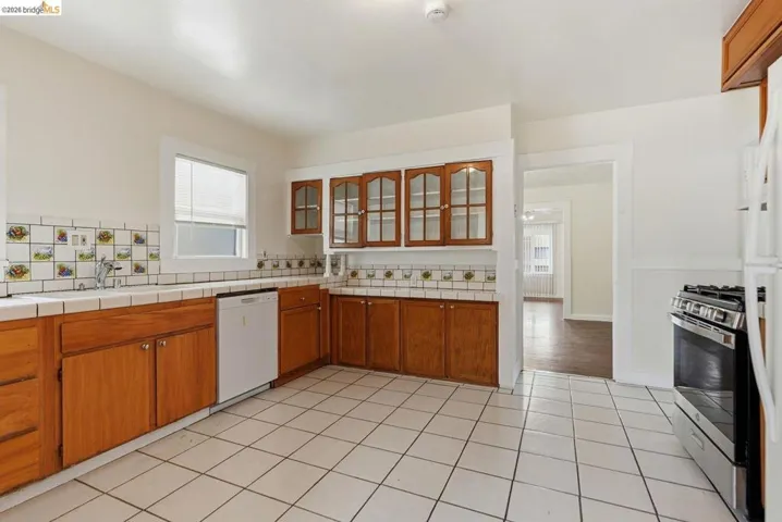 Kitchen featuring white square floor tiles, light wood-finish cabinetry, a white tile countertop, and a decorative tile backsplash