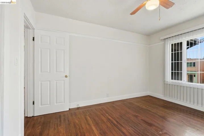 Spacious room featuring wood-finish flooring, a window with vertical blinds, a ceiling fan with integrated lighting, and a six-panel interior door