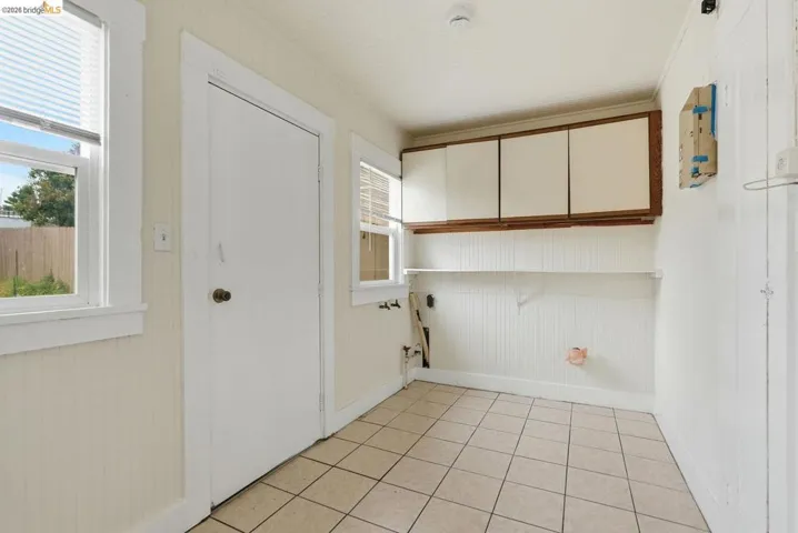 Utility room featuring ceramic tile flooring, beadboard wall paneling, two windows with blinds, built-in upper cabinetry, and shelving