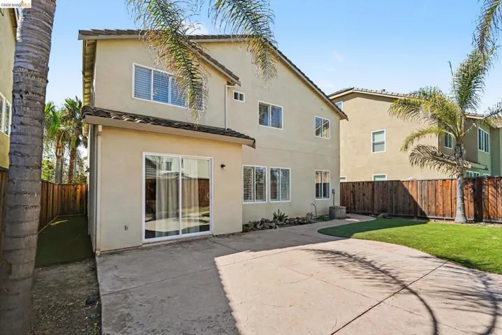 Rear exterior featuring a sliding glass door, multiple windows, a concrete patio, and a grass lawn