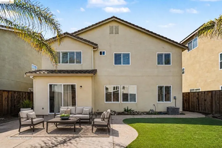 Rear exterior featuring a concrete patio, sliding glass doors, multiple windows with blinds, a stucco finish, and a sloped tile roof