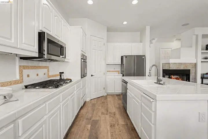 Contemporary kitchen featuring white cabinetry, stainless steel appliances, wood-finish flooring, recessed lighting, and a tile backsplash with decorative accents