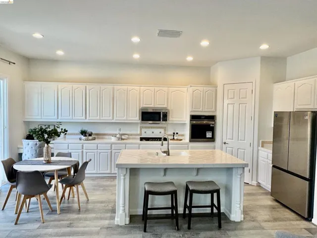 Modern kitchen featuring white cabinetry, stainless steel appliances, a center island with a sink, recessed lighting, and wood-finish flooring